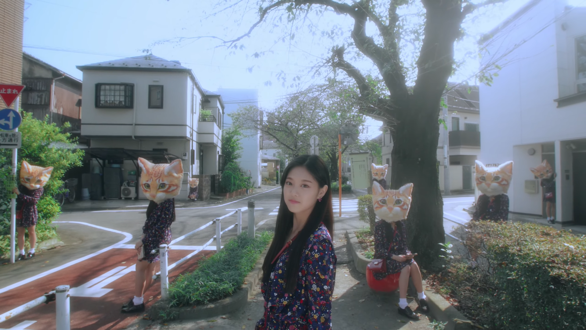 Hyunjin standing in the street from the 'Around You' music video. There are seven clones of her behind her, wearing large orange cat heads.